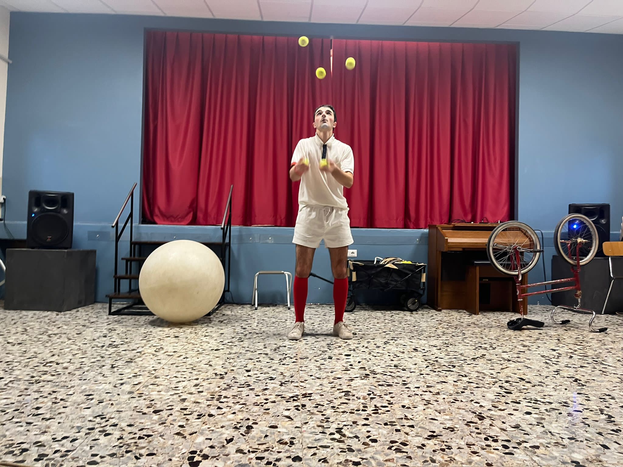 Un clown tennista giocola con 5 palline da tennis.